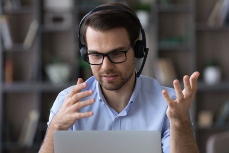 A man wearing headphones and glasses is sitting in front of a laptop computer.