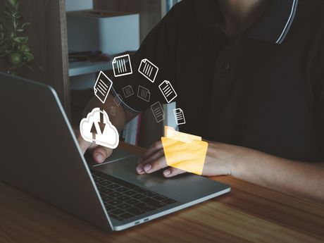 A person is holding a folder in front of a laptop computer.