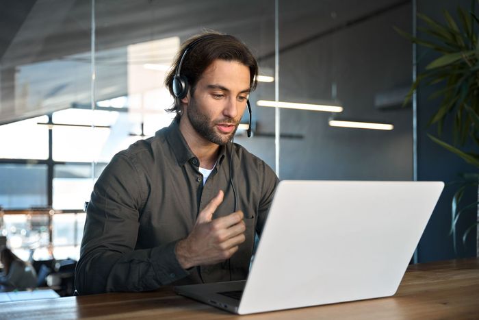 A man wearing headphones is sitting at a table using a laptop computer.