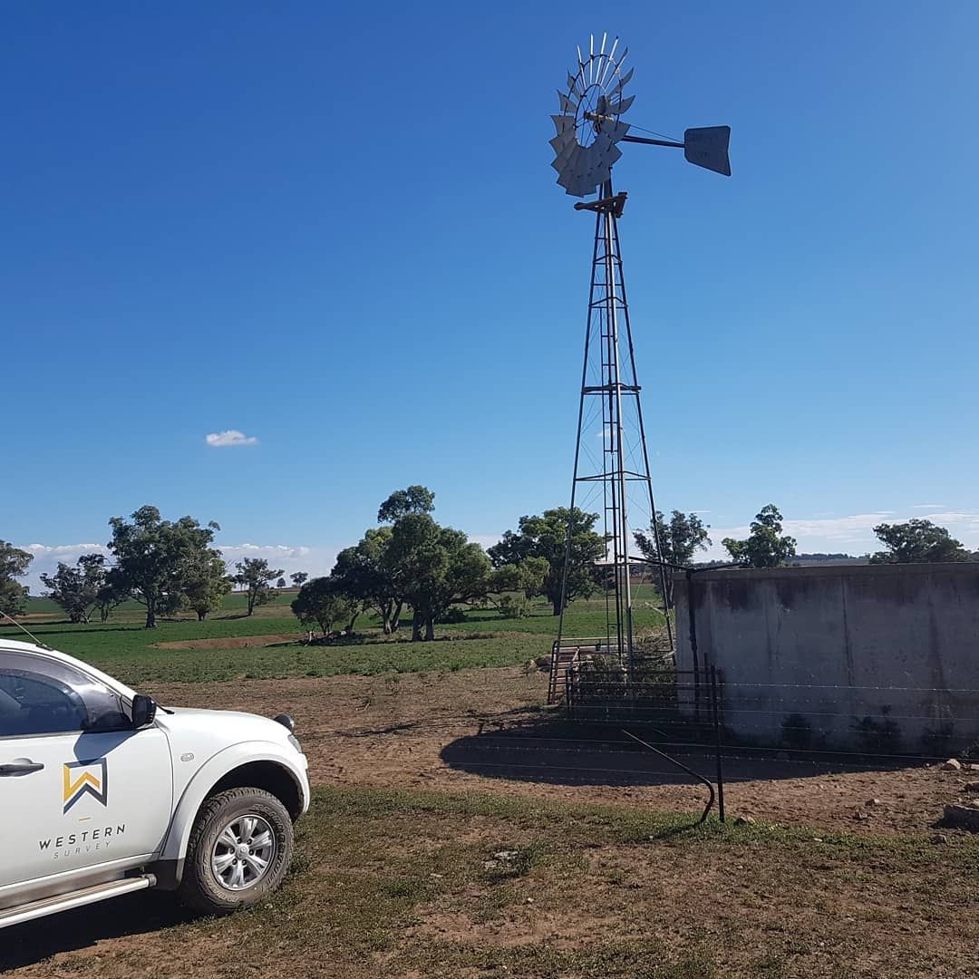 A White Truck Is Parked In A Field Next To A Windmill — Western Survey Pty Ltd In Cowra, NSW