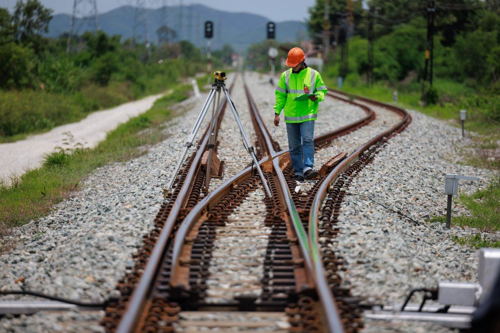 A Man in a Green Vest and Hard Hat is Walking on Train Tracks — Western Survey Pty Ltd In Dubbo, NSW