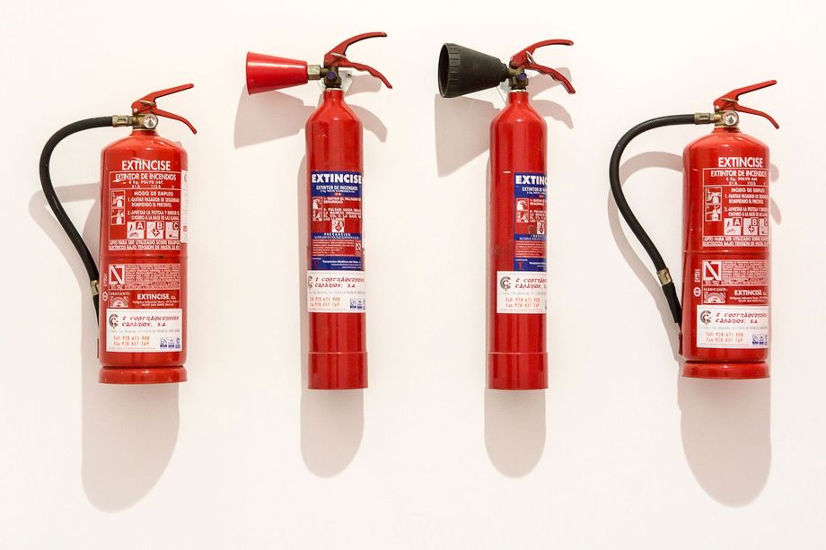 Four red fire extinguishers lined up against a white wall, each with different nozzle styles.