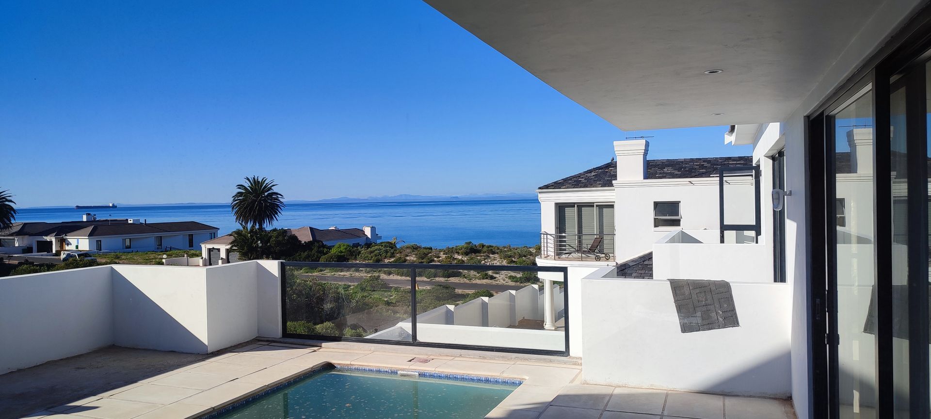 There is a swimming pool in the backyard of a house with a view of the ocean.