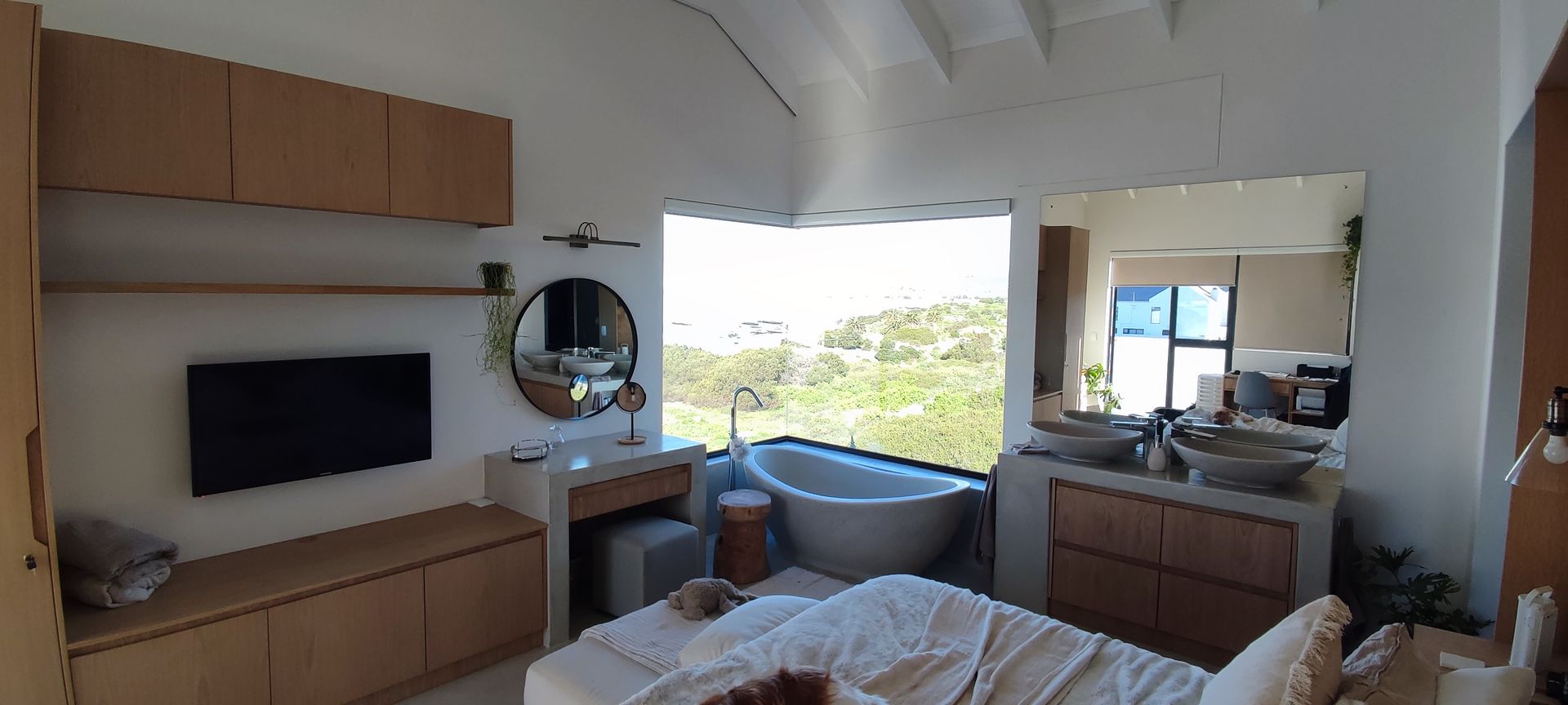 A bedroom with a bed , television , sinks and a bathtub.