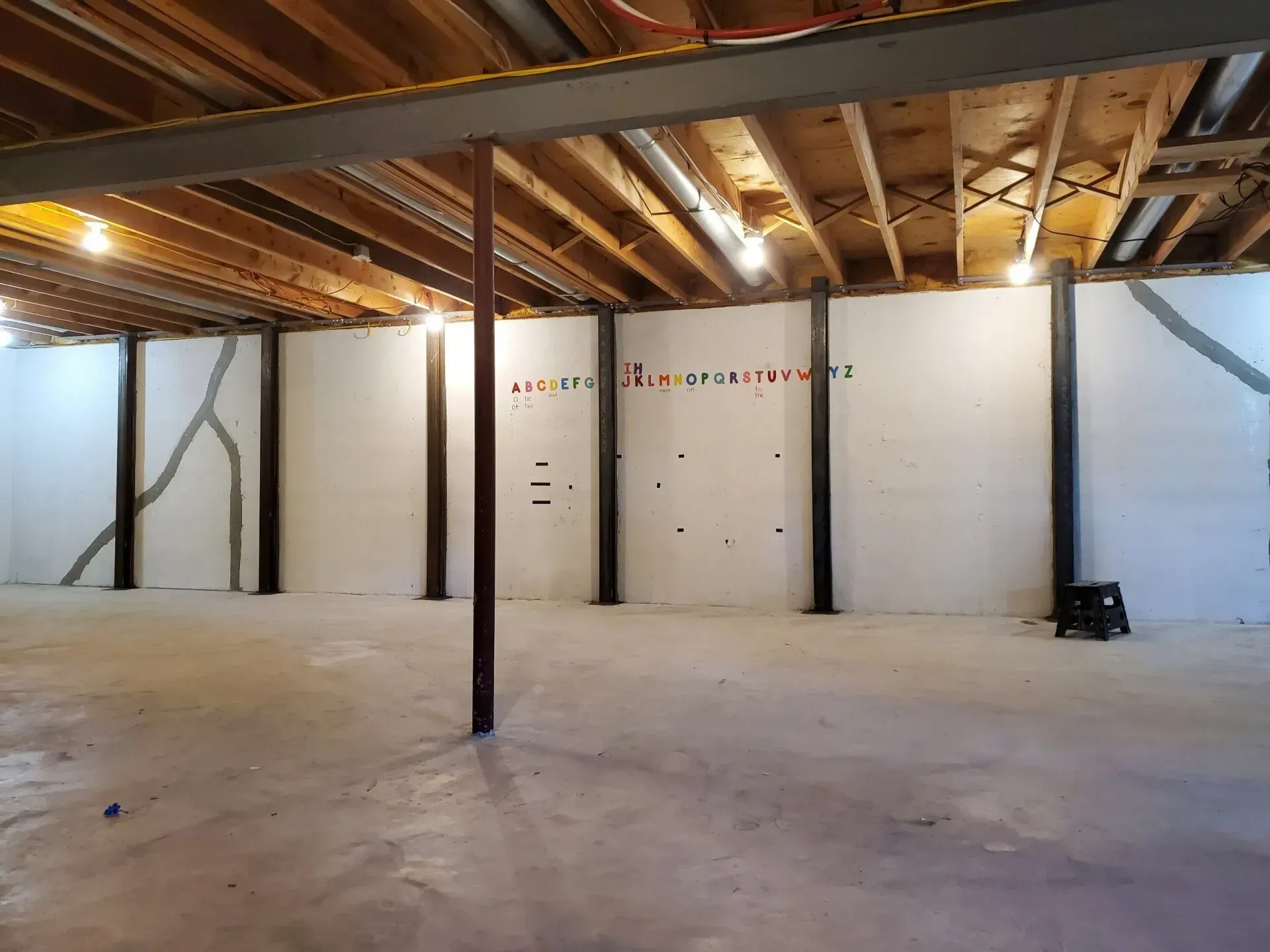 Vertical metal beams brace cracked basement wall with sealed repairs and exposed ceiling. Vertical metal beams brace cracked basement wall with sealed repairs and exposed ceiling.