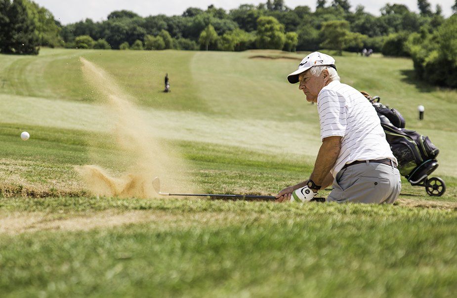 A man is kneeling down on a golf course playing golf.