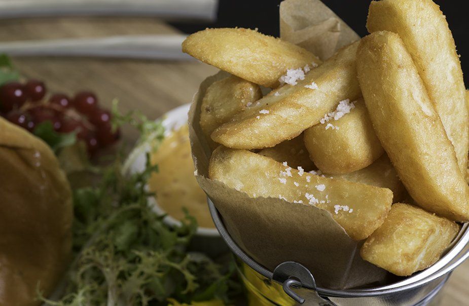 A bucket of french fries is sitting on a table next to a hamburger.