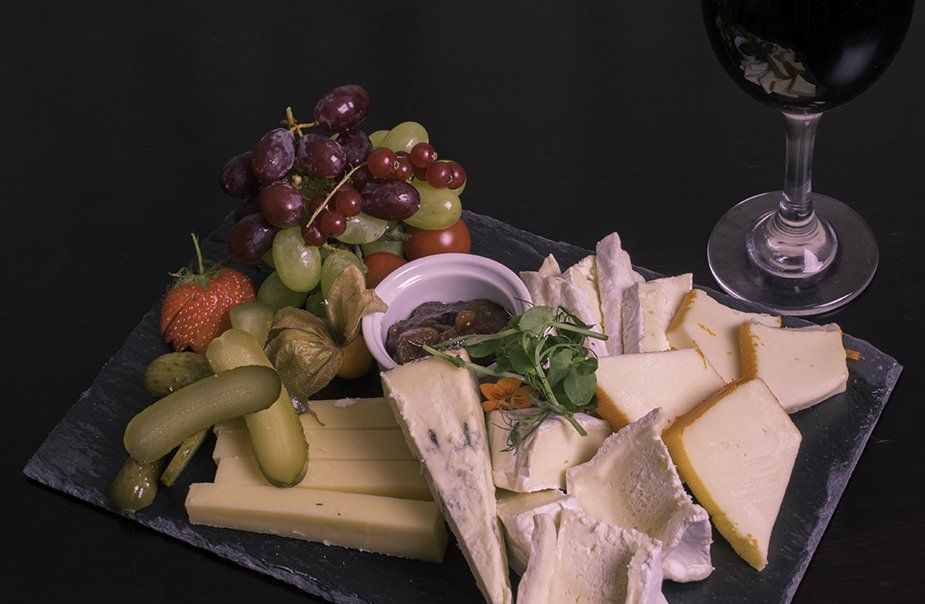 A plate of cheese , grapes , pickles and a glass of wine on a table.