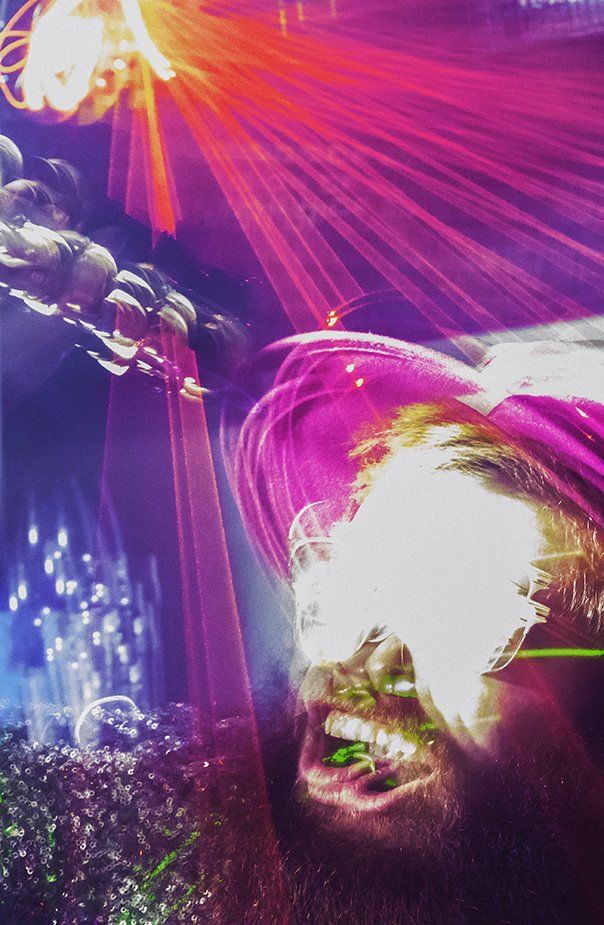 A man with purple hair is laying on his back in a dark room