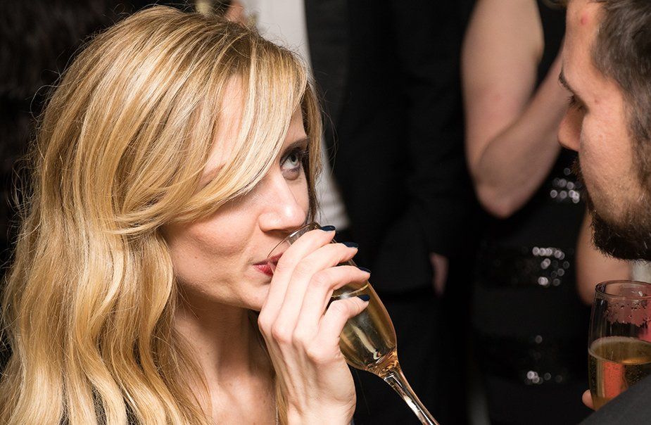 A woman is drinking champagne from a glass while talking to a man.