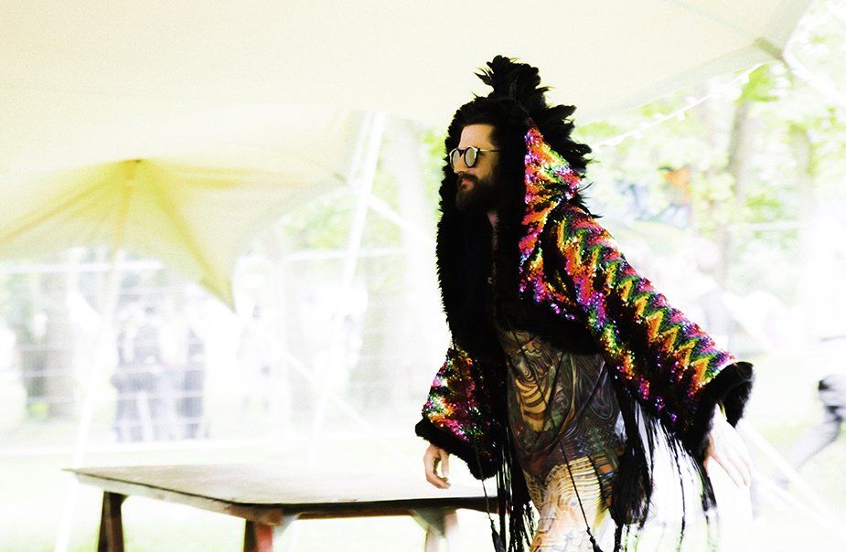 A man with a beard and glasses is standing next to a table.