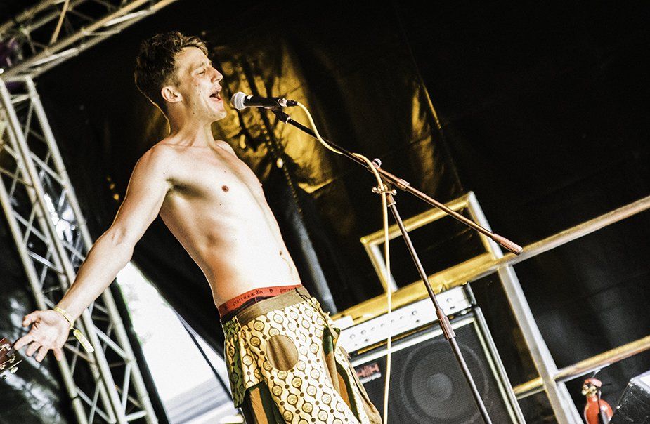A shirtless man is singing into a microphone on a stage.