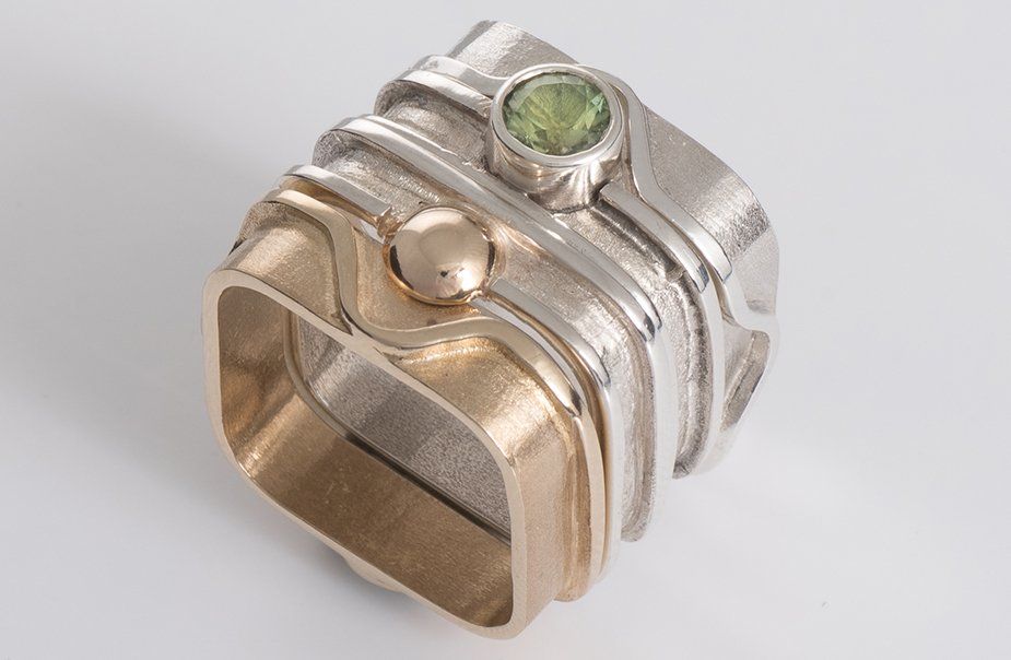 A silver and gold ring with a green stone in the center