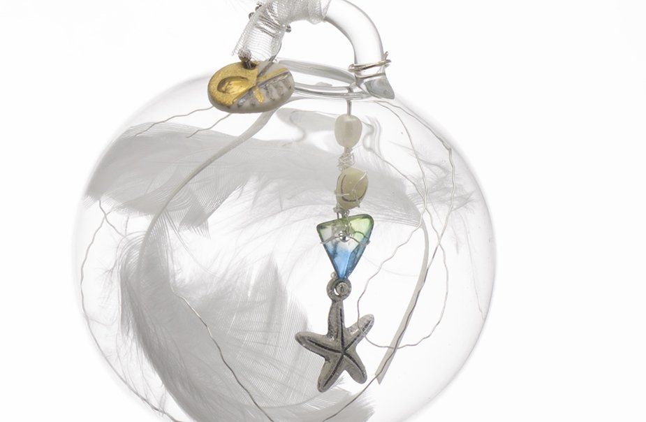 A clear glass ball with feathers and a starfish hanging from it.