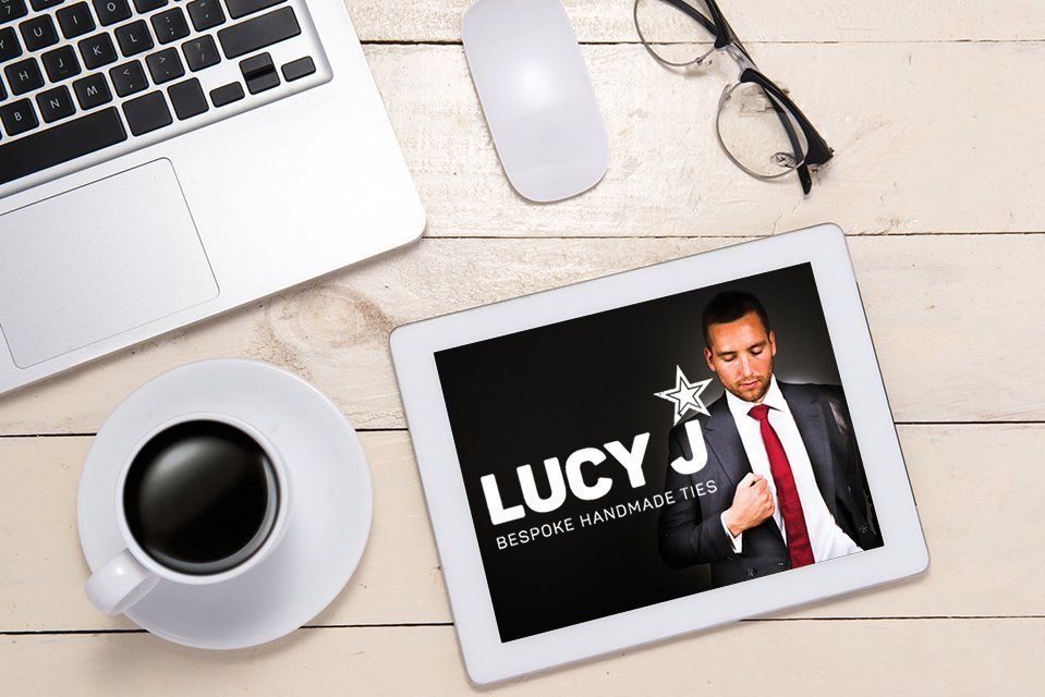 A man in a suit and tie is on a tablet next to a cup of coffee and a laptop.
