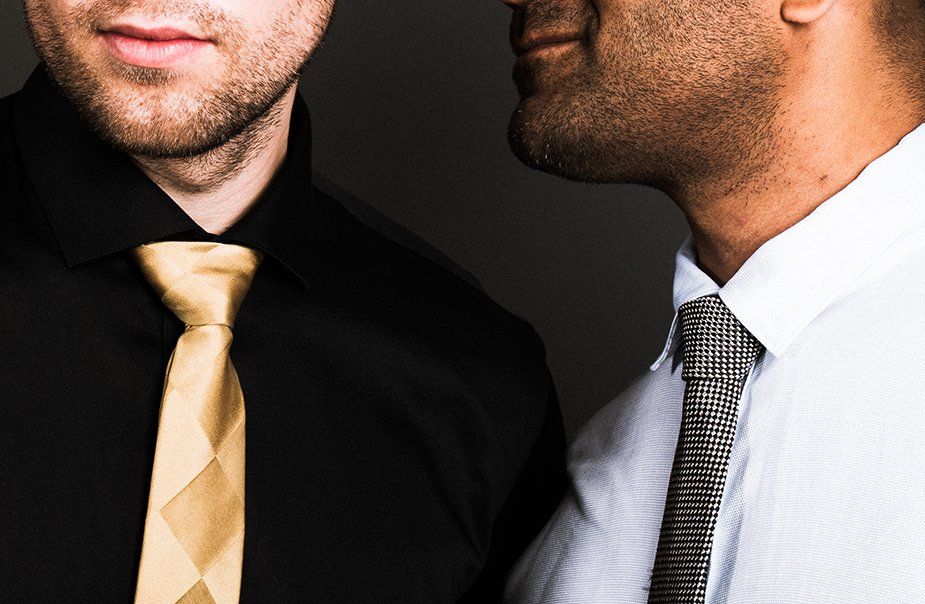 Two men are standing next to each other and one is wearing a gold tie