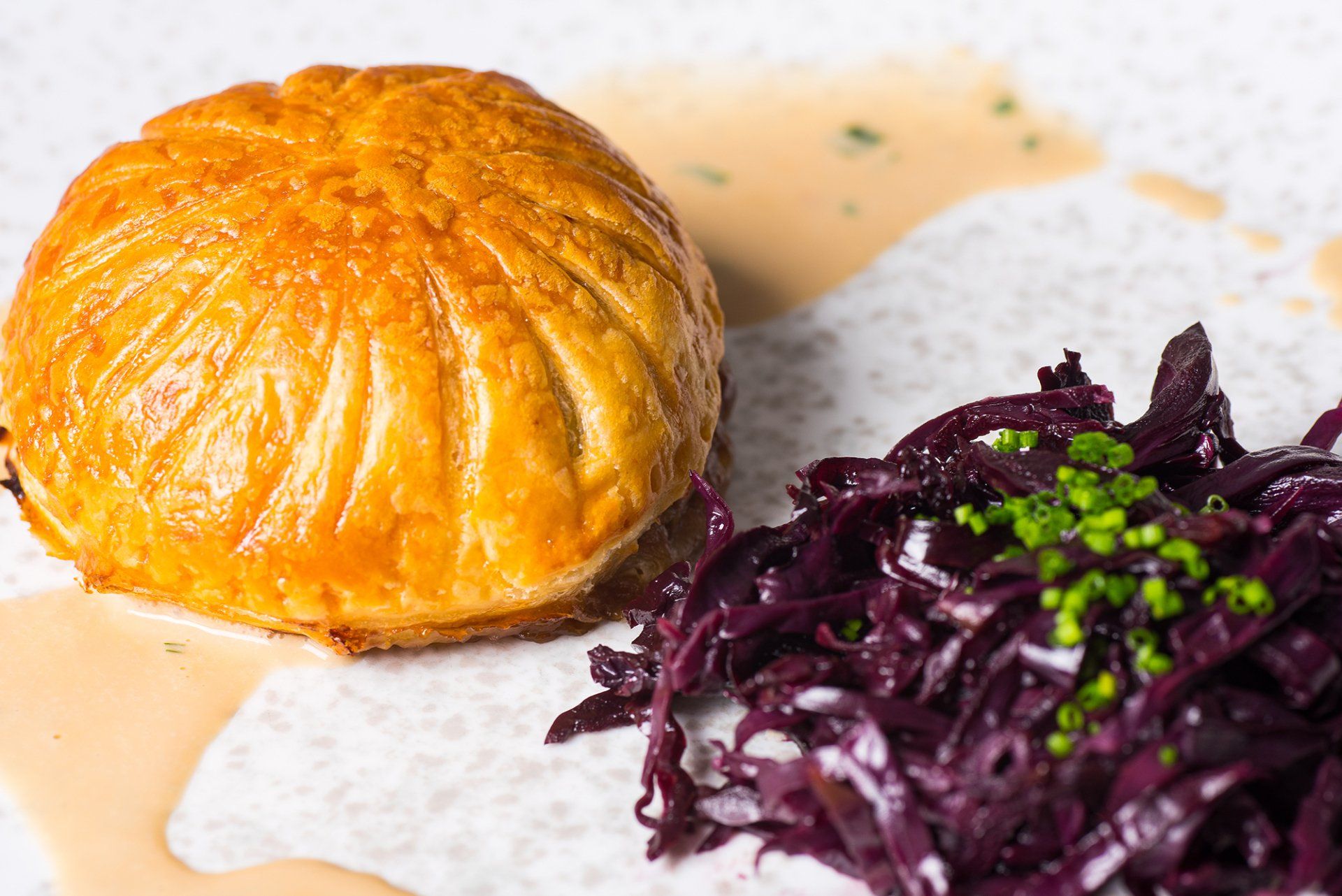 A close up of a plate of food with a pastry and red cabbage.
