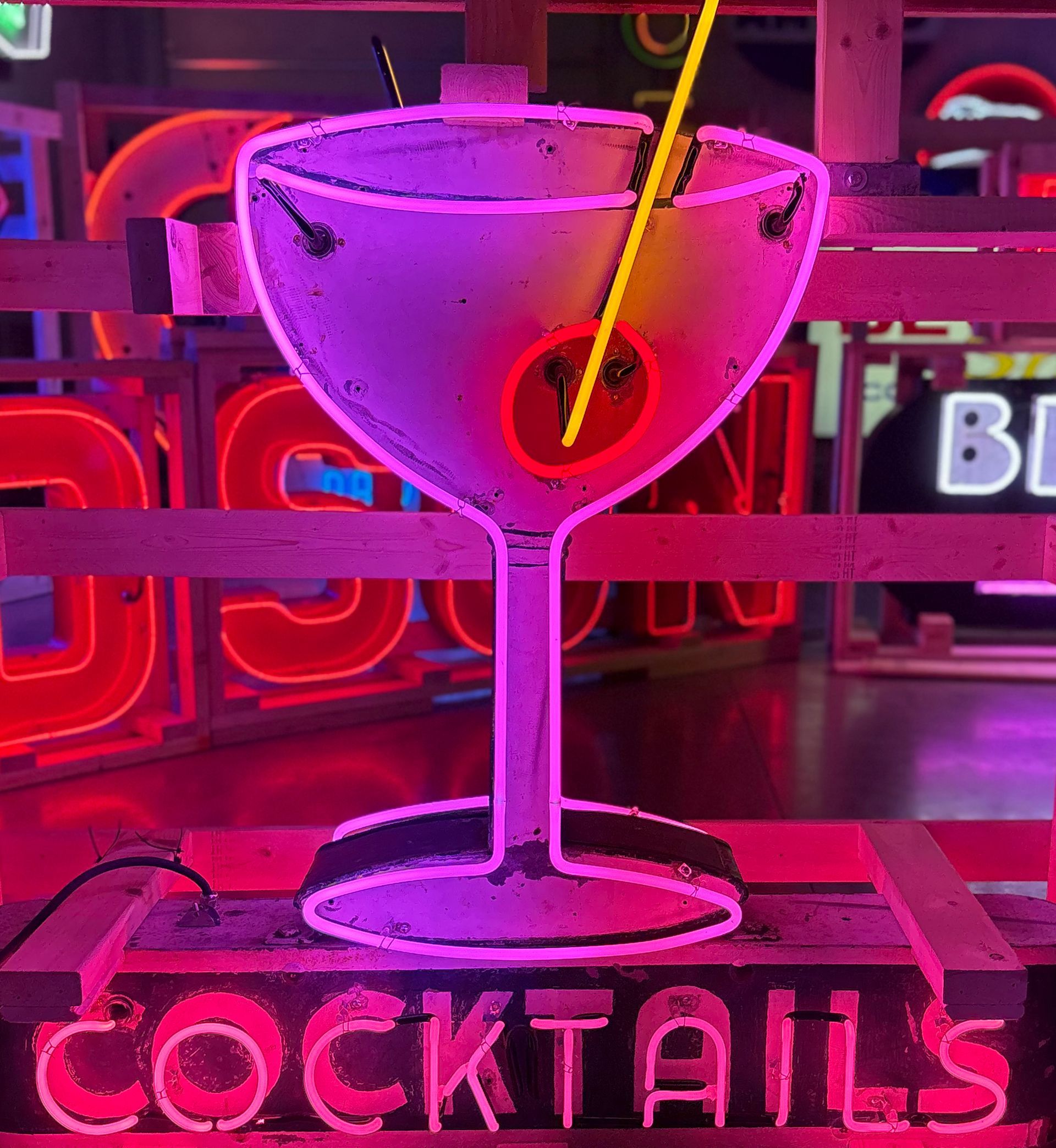 Neon sign of a martini glass, lit in pink and purple, with the word 