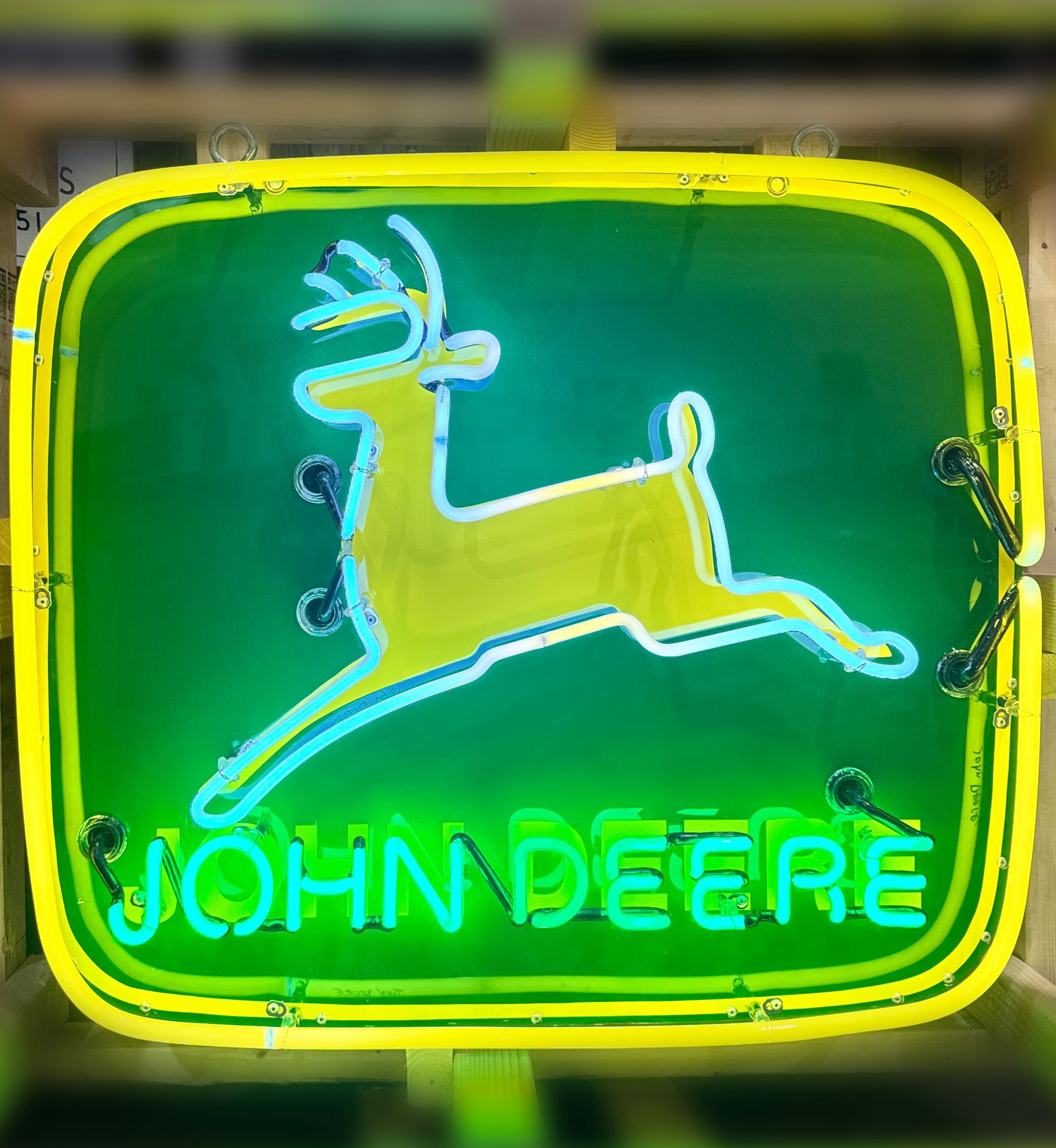 Neon sign: John Deere logo with a yellow deer on a green background, outlined in green neon.