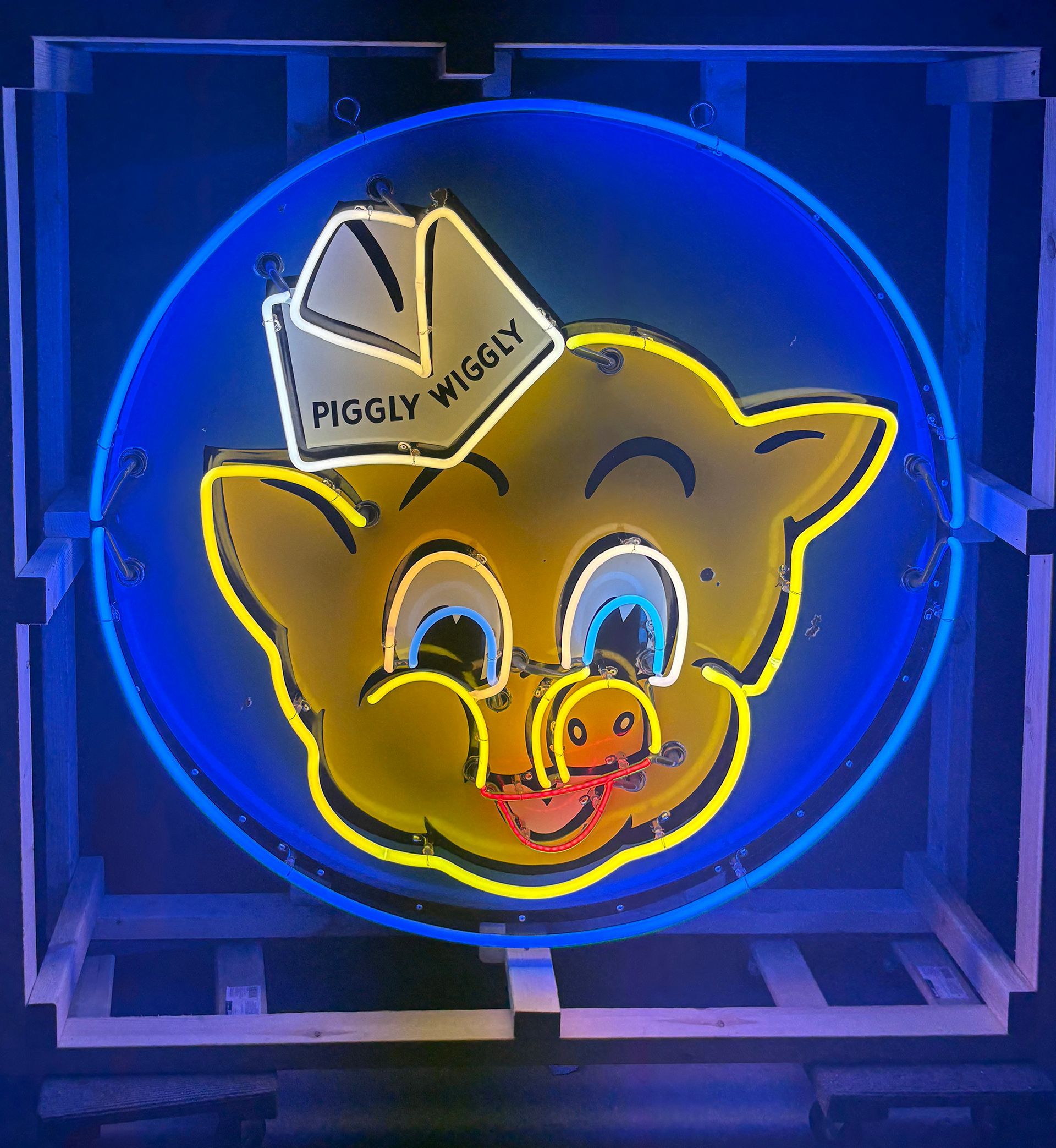 Neon sign of a yellow pig with a chef hat, inside a blue circle. Piggly Wiggly logo.