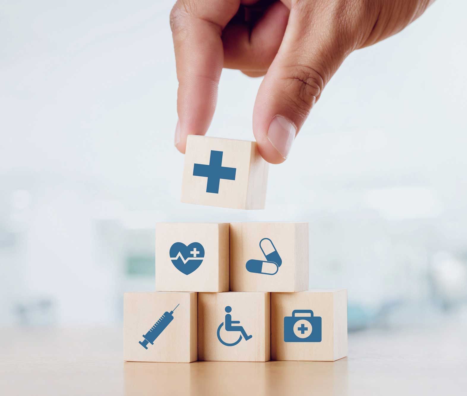 A hand is stacking wooden blocks with medical icons on them.
