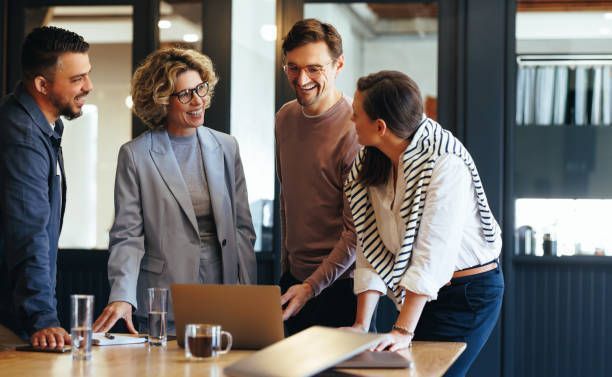 A group of people are standing around a table looking at a laptop.