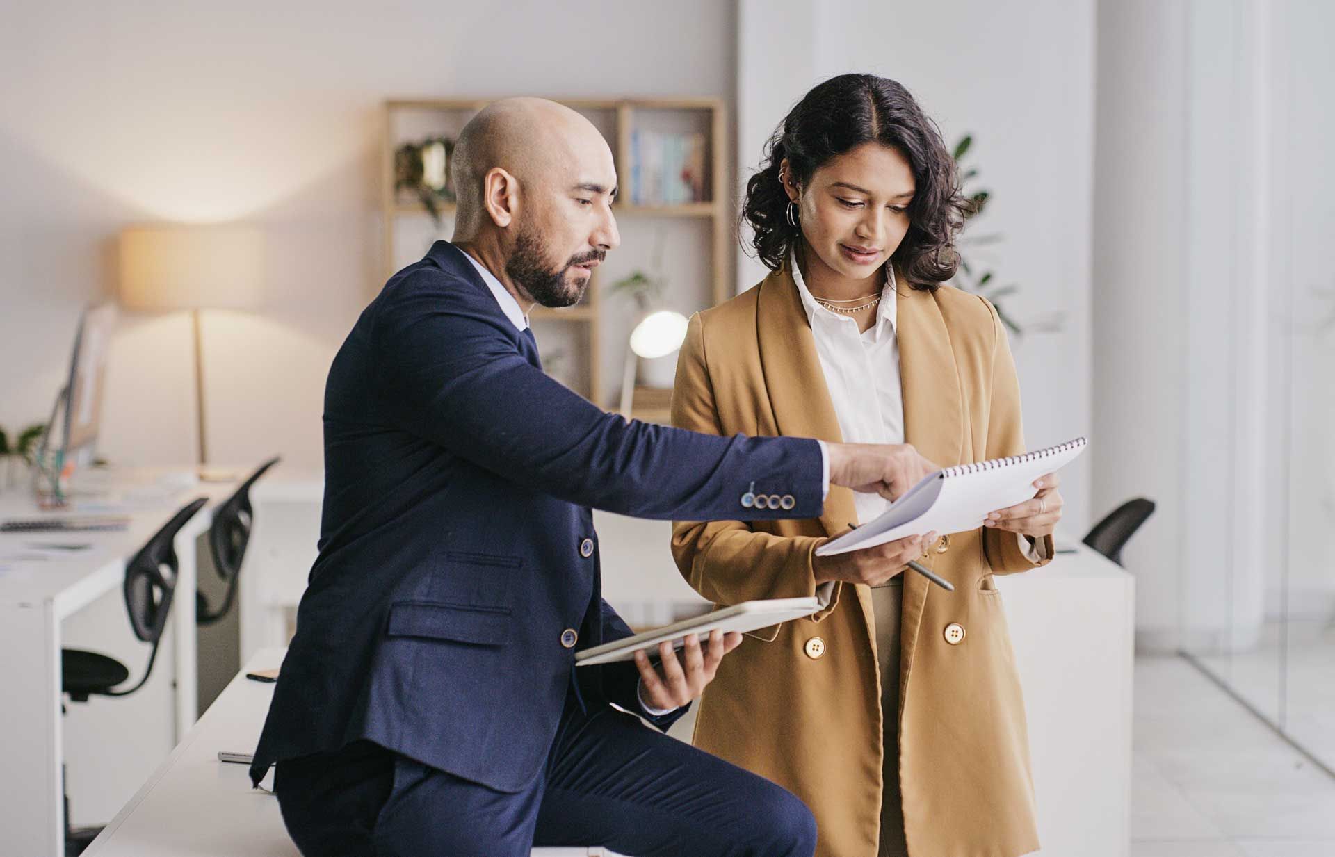 A man and a woman are looking at a piece of paper in an office.