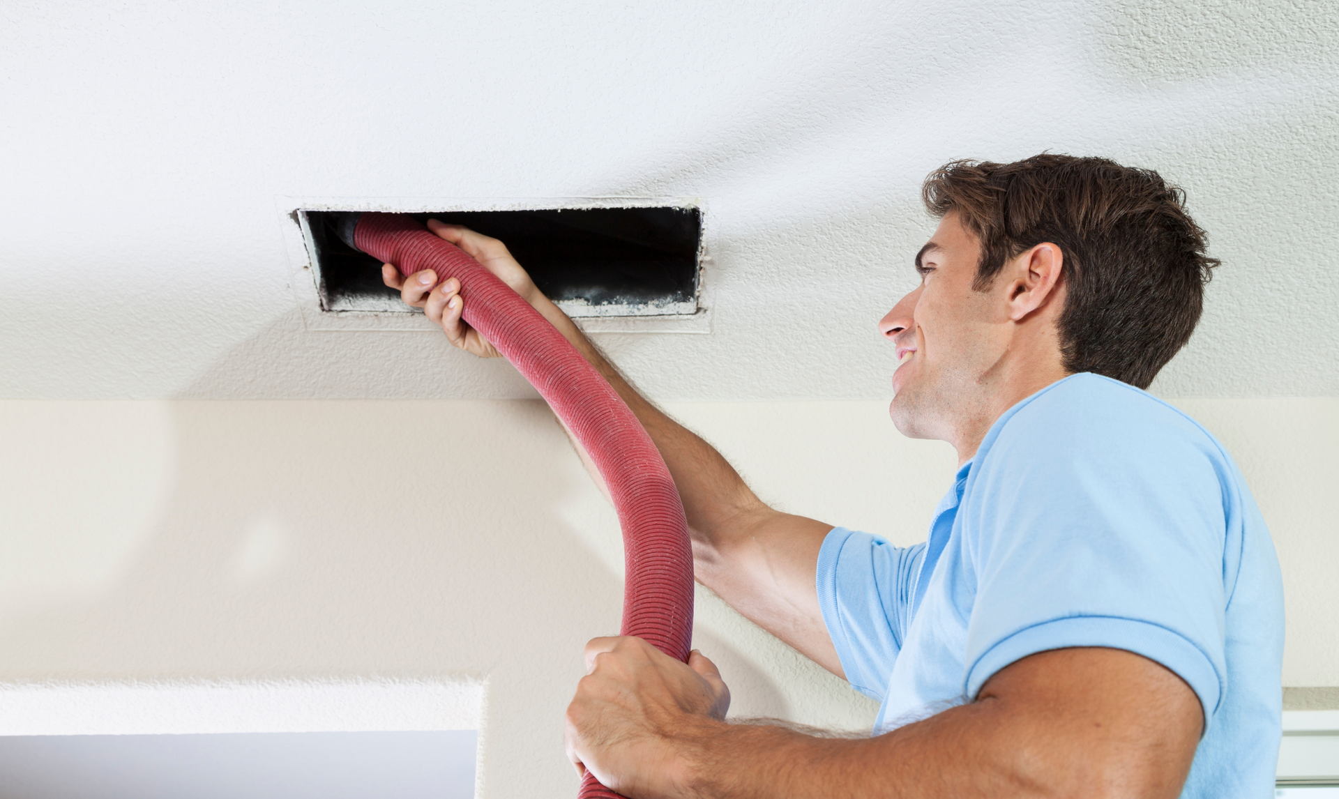 A man is using a vacuum cleaner to clean an air vent.
