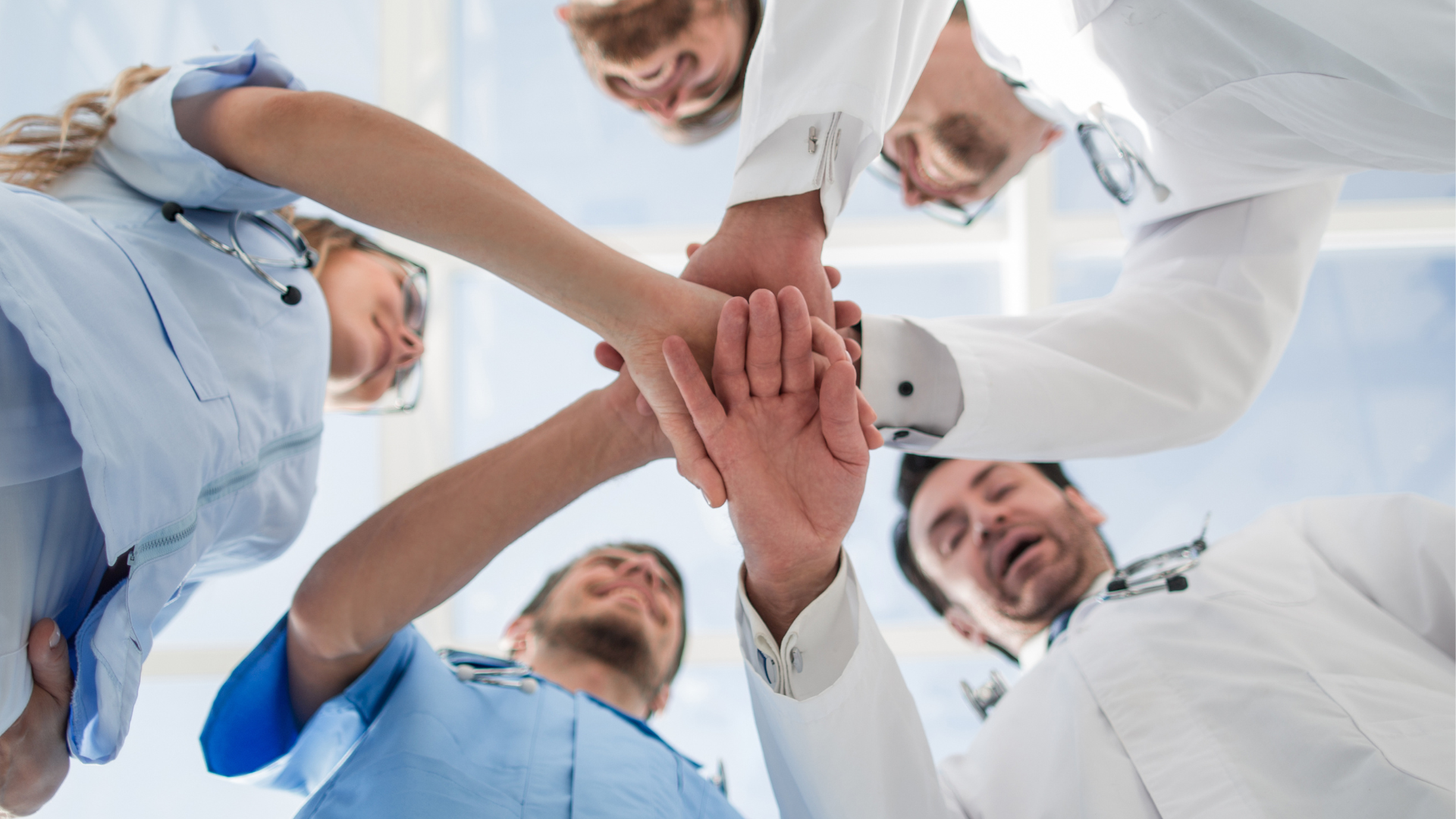 A group of doctors and nurses are putting their hands together in a circle.