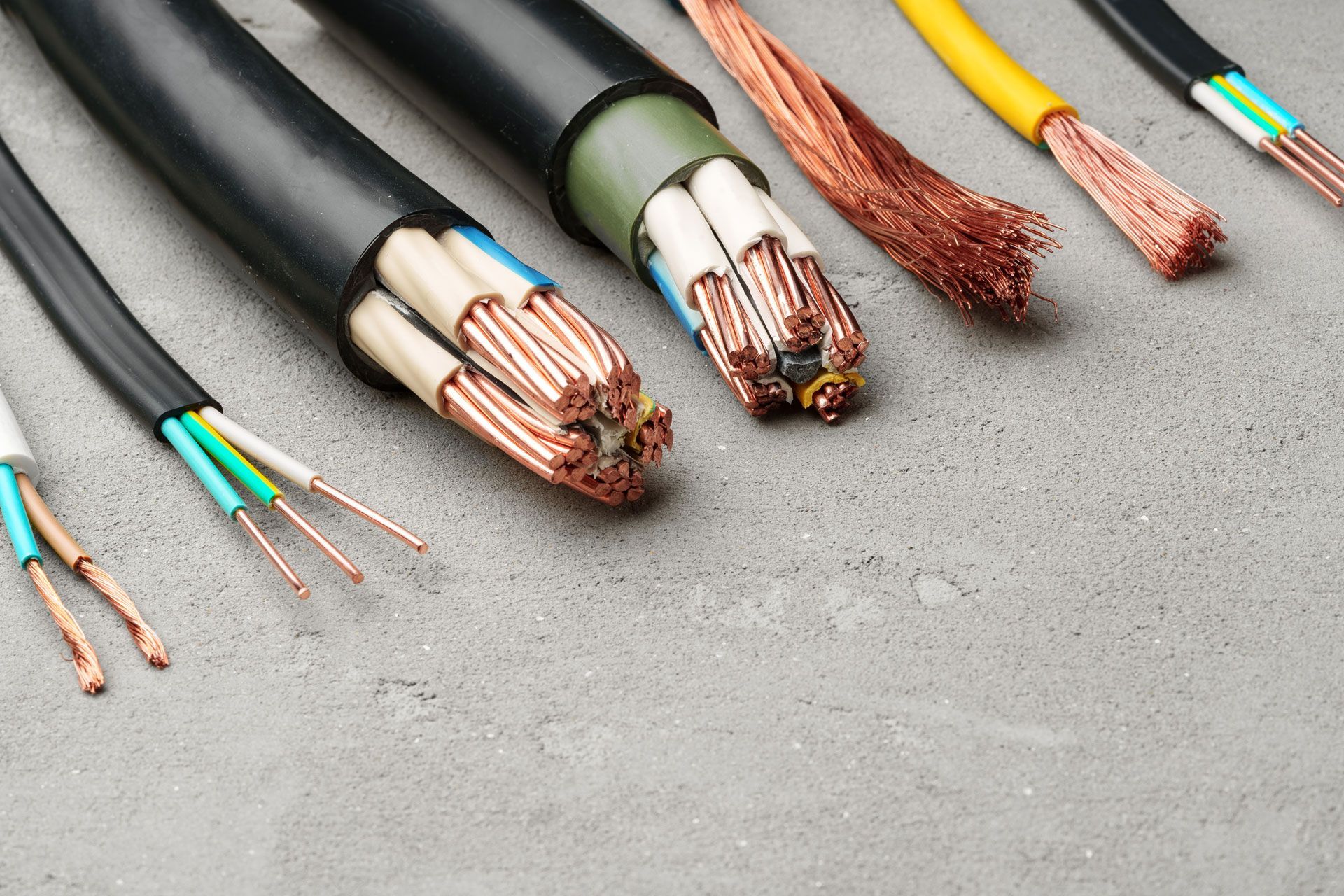 Various electrical cables with exposed copper wires on a grey surface.