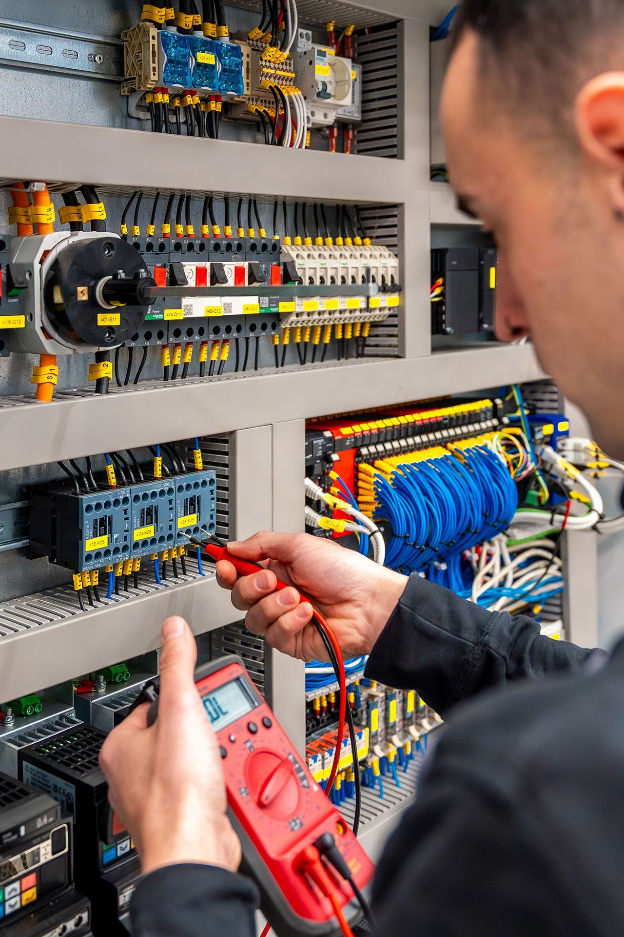 Electrician uses multimeter to test wires inside a control panel.