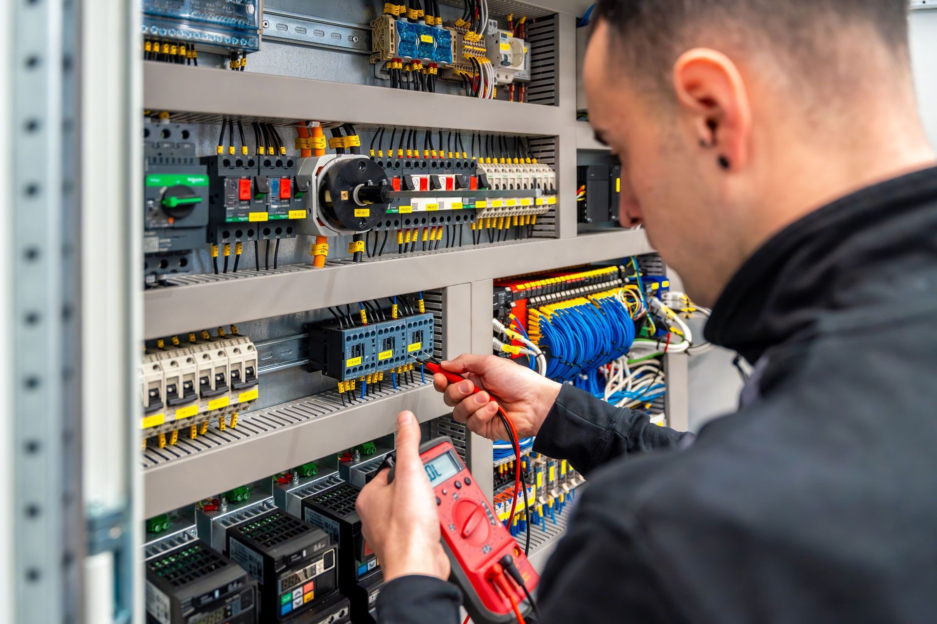 Electrician using a multimeter to inspect wiring in a control panel.