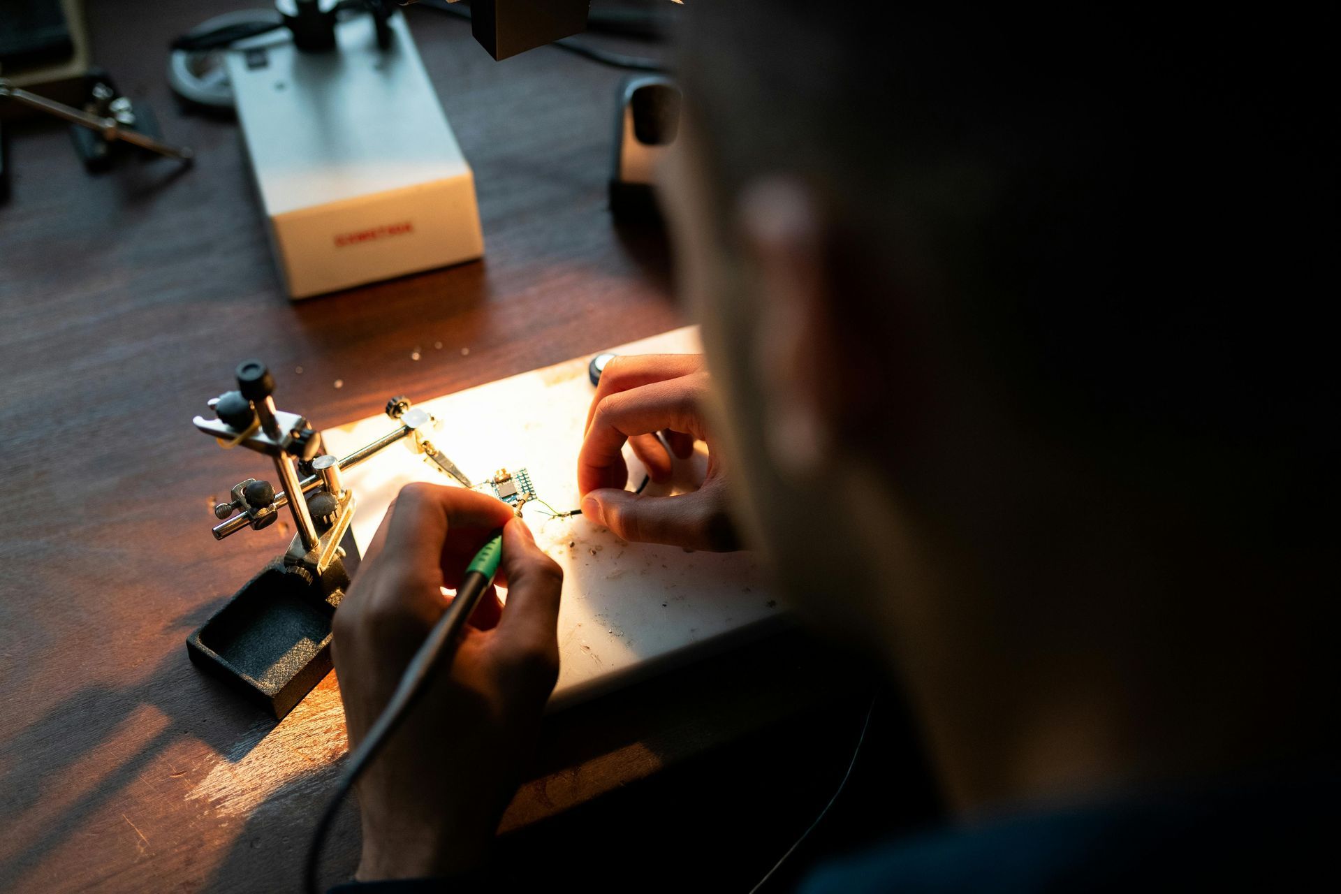 Person soldering circuit board, hands close up. Solder iron, small parts on a table.