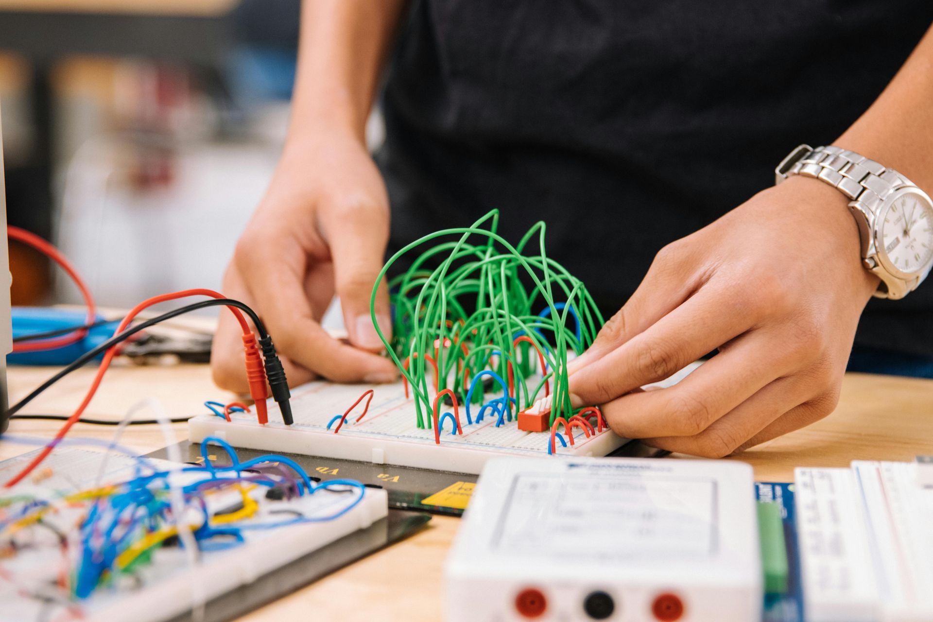 Hands working on a breadboard circuit with green wires and other electronic components.