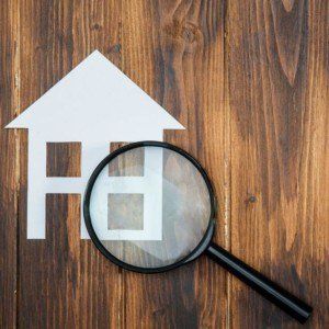 A magnifying glass is looking at a paper house on a wooden table.