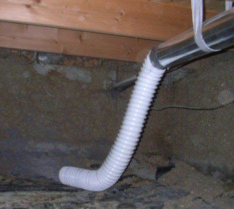 A white hose is attached to a metal pipe in a basement.
