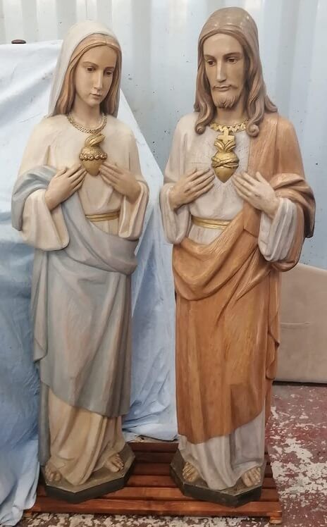 Statue di Gesù e Maria; entrambi indossano tuniche e mostrano cuori fiammeggianti; materiale in legno, ambientazione interna.
