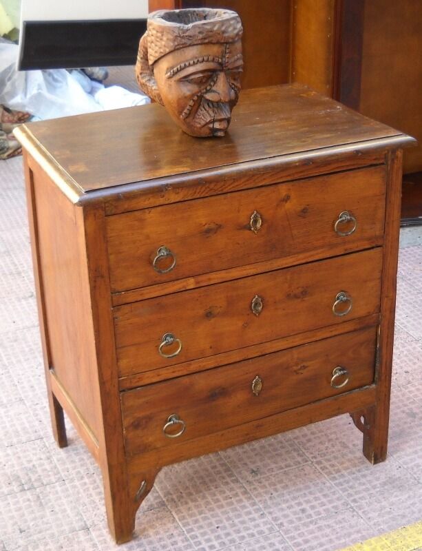 Cassettiera in legno con tre cassetti, maniglie in ottone e un volto intagliato sulla parte superiore.