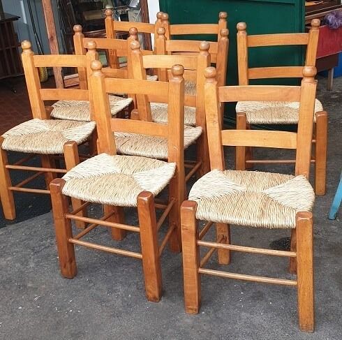 Otto sedie in legno con seduta intrecciata, disposte all'esterno.