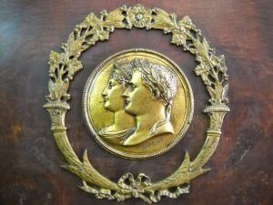 Medaglione dorato con due profili, incorniciato da una corona d'alloro su una superficie di legno.