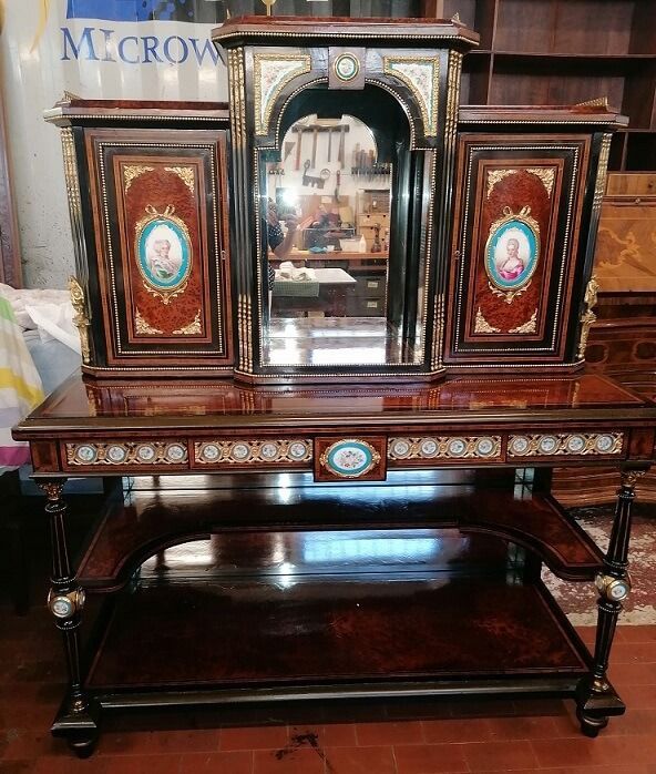 Mobiletto antico in legno scuro con dettagli decorati, specchio e pannelli decorativi.