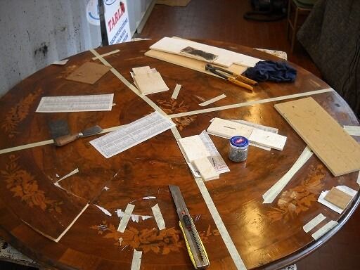 Tavolo rotondo in legno in fase di riparazione, sezioni nastrate con attrezzi e pezzi di legno sparsi sulla parte superiore.