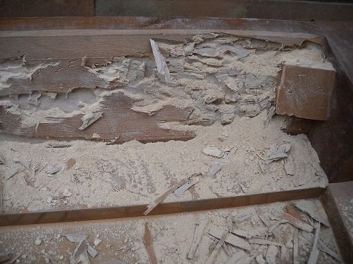 Telaio in legno gravemente danneggiato da detriti polverosi e strati scrostati.