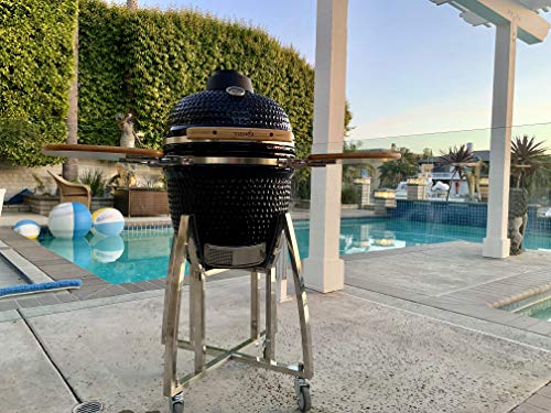 Un barbecue en céramique noire en forme d'œuf repose sur un cadre métallique roulant, sur une terrasse à côté d'une piscine dans le jardin.
