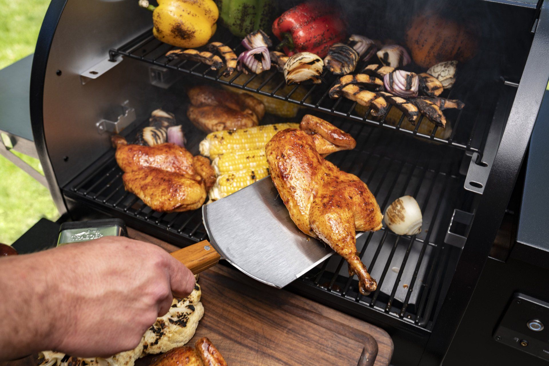 Une personne utilise une spatule métallique pour transférer un quart de poulet cuit d'un barbecue de jardin à une planche à découper en bois.