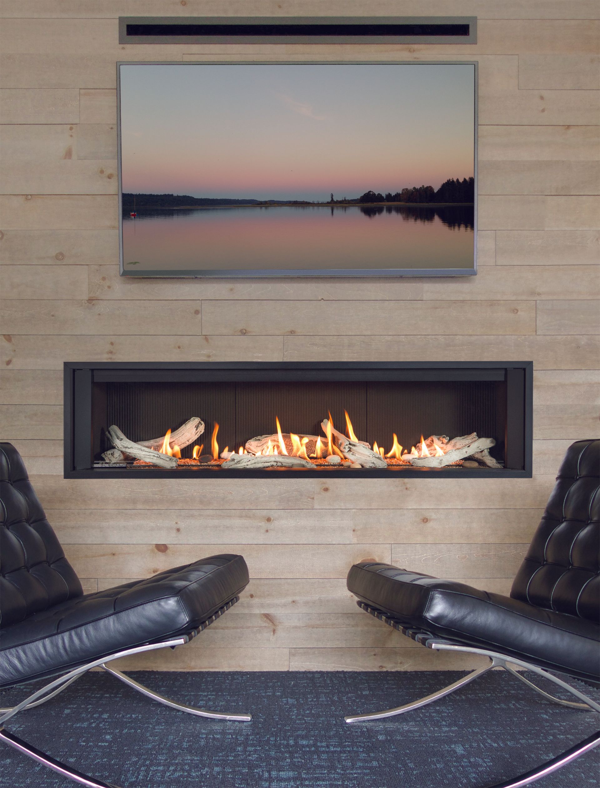 Deux fauteuils en cuir noir font face à une cheminée linéaire moderne surmontée d'une télévision, le tout adossé à un mur lambrissé clair.