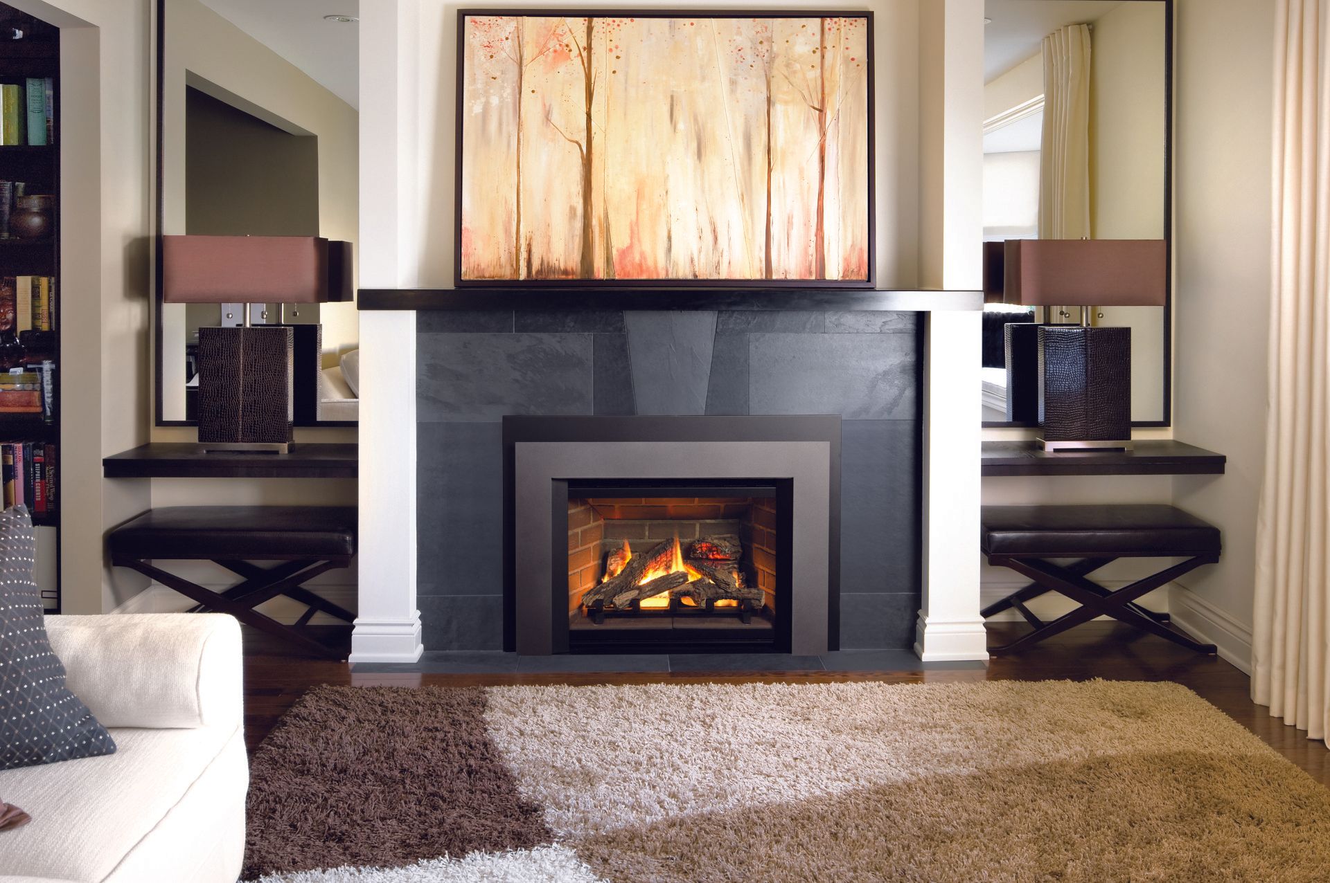 Une cheminée avec un contour noir et des flammes, flanquée d'étagères en miroir avec des lampes et un tableau au-dessus.