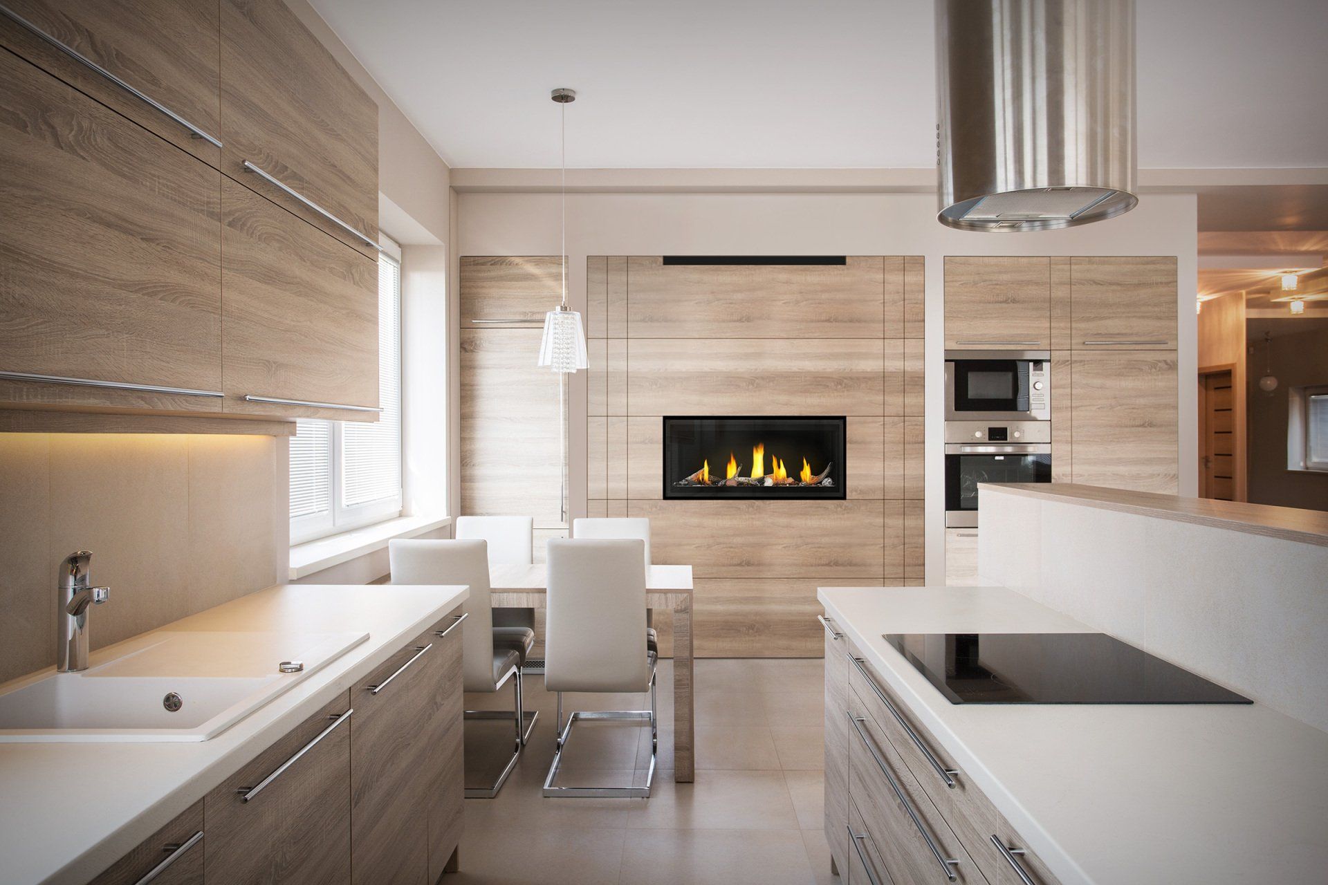 Une cuisine et une salle à manger modernes avec des armoires en bois clair, des comptoirs blancs, une cheminée et un ensemble de salle à manger blanc.