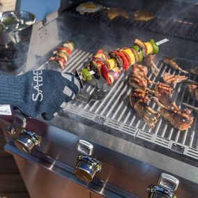 Une personne portant un gant de sabre fait cuire des aliments sur un gril.