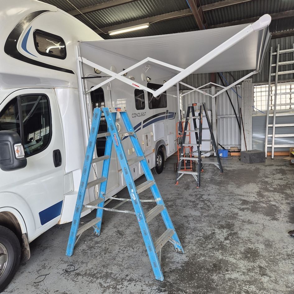 A white campervan with an extended awning. Two ladders stand near the van, inside a garage  — Revive Caravan Repairs in Kippa-Ring, QLD